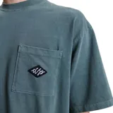 Remera de algodón color verde azulado con efecto lavado, corte holgado y bolsillo frontal con un pequeño bordado en forma de diamante.