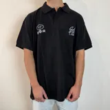 Chomba negra de corte oversize con cuello clásico y cierre de botones. Presenta bordados en blanco en el frente.