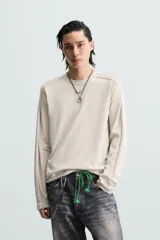 Camiseta color beige de corte relaxed fit, con cuello redondo y mangas largas combinadas con tejido de red.