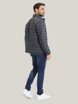 Chaqueta acolchada gris de poliamida con cuello alto, cierre de cremallera, dos bolsillos delanteros con cremallera y logo de Tommy Hilfiger bordado en el pecho.
