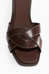 Sandalias de cuero color marrón con punta cuadrada y tiras anchas trenzadas. Tienen un taco de 1 cm y costuras blancas a contraste.