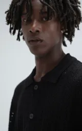 Camisa negra de tejido de punto calado con diseño de zigzag, cuello polo, manga corta y cierre frontal con botones.