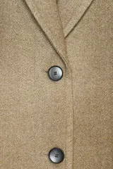 Abrigo largo color beige, de cuello solapa y manga larga con hombreras. Tiene bolsillos con solapa en la parte delantera y cierre frontal con botones.