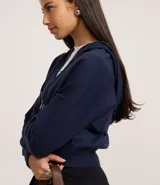 Campera corta de mujer con capucha ajustable con cordón, cierre frontal de cremallera y puños y bajo ajustados. Confeccionada en tejido de punto.