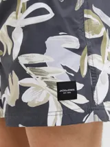 Short de baño con estampado floral en tonos blanco, verde y marrón sobre fondo azul oscuro. Cuenta con cintura elástica, cordón ajustable, bolsillos laterales y trasero.