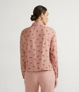 Camisa de viscosa color rosa con estampado de caballos en marrón. Tiene cuello camisero, cierre con botones, mangas largas, un bolsillo frontal y detalle de vivo contrastante.