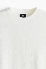 Remera blanca de punto texturizado de peso medio, corte estándar, cuello redondo y mangas cortas.
