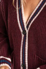 Cardigan de lana color bordó con cuello V y botones frontales. Presenta ribetes en el cuello, puños y ruedo con rayas en color beige y azul marino. Posee dos bolsillos frontales.