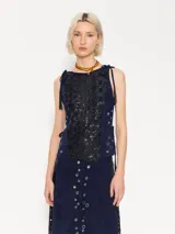 Top corto sin mangas de gamuza azul marino con tela bordada con lentejuelas en el frente. Breteles que se anudan sobre los hombros y ojalillos metálicos en los laterales con tiento de gamuza para ajustar la cintura. Cierre metálico en la espalda.