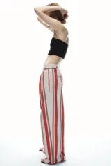 Pantalón de tiro medio con estampado de rayas verticales negras sobre fondo blanco. Tiene trabillas en la cintura, bolsillos laterales, pinzas delanteras y cierre frontal con cremallera, botón y ganchos metálicos.