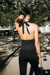Chaleco negro con estampado de lunares blancos, escote en V, cuello halter con lazo y cierre frontal con botones.
