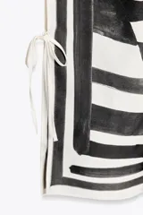 Pantalón de tiro medio con cintura elástica y pierna ancha. Presenta un estampado de líneas onduladas en blanco y negro, y aberturas laterales ajustables con lazadas.