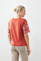 Remera color ladrillo con bordado de flores blancas en el ruedo y las mangas.