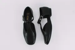 Zapato flat de cuero con estampado de vaca en blanco y negro, con tira delantera y hebilla lateral.