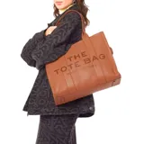 Bolso tote grande de cuero color camel, con textura granulada y asas de hombro. Presenta el texto en relieve "THE TOTE BAG" y debajo "MARC JACOBS" en color marrón oscuro.
