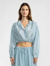 Blusa corta celeste en tejido arrugado liviano, con cuello mao, botones al frente, mangas abullonadas y ruedo elastizado.