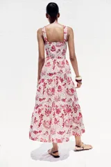Vestido midi con estampado floral en tonos rosados, de escote recto y tirantes anchos con abalorios. Presenta aberturas laterales en la cintura y cierre trasero con cremallera oculta.