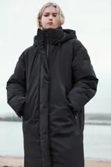 Anorak largo negro resistente al agua y al viento, con aislamiento térmico, cuello alto con capucha ajustable, bolsillos con cremallera, acolchado interior, tirantes elásticos y cremalleras laterales en el bajo.