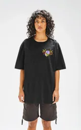 Remera negra de corte oversize con hombros caídos y cuello redondo. Estampado en la espalda con una mano que exprime un jugo sobre una persona rodeada de plantas de marihuana.