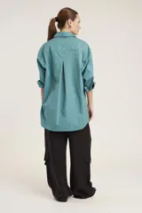 Camisa blanca de corte clásico con cuello abotonado, cierre frontal con botones y mangas largas con puños abotonados. Presenta pequeños apliques de strass plateados dispersos por toda la prenda.