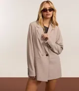 Blazer largo color beige, de corte recto, con cuello solapa, cierre frontal con doble botón, bolsillos tipo ojal y mangas largas con botones decorativos en los puños.