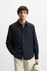 Camisa azul marino de corte regular fit, confeccionada en tejido de algodón con estructura. Tiene cuello solapa, manga larga con puños abotonados y cierre frontal con botones.