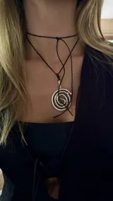 Colgante de metal plateado con diseño de espiral concéntrico, atado a un cordón negro de seda ajustable.