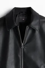 Campera negra de cuero sintético, con cuello clásico, cierre frontal con cremallera, bolsillos laterales con botón a presión, bolsillo interior y puños con botón.