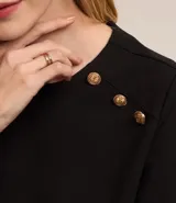 Blusa negra de crepé con cuello redondo, mangas cortas y botones decorativos dorados en los hombros.