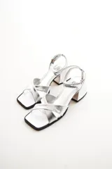 Sandalias plateadas de cuero, con tiras cruzadas sobre el empeine, pulsera al tobillo con hebilla y taco bajo cuadrado.