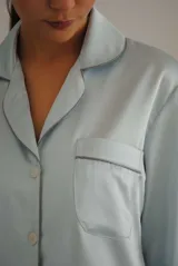 Pijama de satén celeste con vivos en contraste. Incluye camisa de manga larga con botones y pantalón recto con elástico y lazo en la cintura.