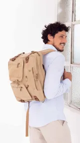 Mochila de tela canvas color beige con detalles en cuero marrón. Cuenta con múltiples bolsillos con cierre, compartimento acolchado para notebook y correas ajustables.