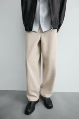 Pantalón chino color beige, de corte relaxed fit, confeccionado en tejido de mezcla de algodón y lino. Cuenta con bolsillos delanteros y traseros de vivo. Cierre frontal con cremallera y botón.