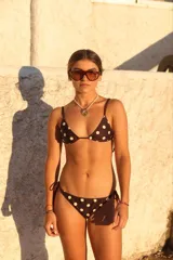 Conjunto de bikini negro con estampado de lunares blancos. El corpiño es triangular y regulable, y la bombacha es semi-vedetina con tiras laterales ajustables.