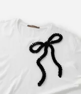 Remera blanca de algodón con cuello redondo, mangas cortas y aplicación de cinta contrastante formando un lazo negro en el frente.