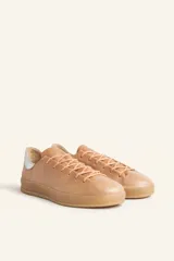 Zapatillas bajas blancas de cuero vacuno con detalle de refuerzo de gamuza color borgoña en el talón y suela de goma color caramelo.