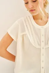 Camisa negra de manga corta con combinación de tejido de punto y plano, detalles de volados y frunces en pechera y espalda, acceso con botones fake nacar y medallita marcaria en espalda.