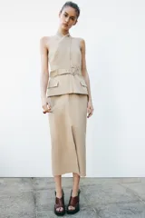 Vestido midi color beige con cuello halter cruzado, cinturón con hebilla y bolsillos tipo parche.