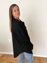 Sobrecamisa negra de pana fina con algodón, corte relajado, largo asimétrico, bolsillos delanteros y cierre de botones.