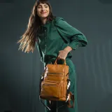 Mochila de símil cuero color marrón con apertura superior y tres bolsillos frontales con cierres metálicos. Cuenta con bolsillos laterales, compartimentos internos y una correa de galón regulable con diseño geométrico para utilizar como bandolera.