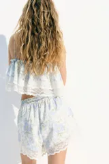 Short blanco con estampado floral celeste y verde, tiro alto, corte holgado, elástico en la cintura y ribete de encaje en el bajo.