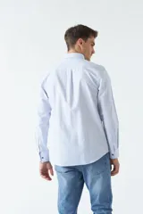 Camisa oxford celeste con rayas verticales blancas, de manga larga y corte regular. Tiene cuello abotonado, bolsillo en el pecho y logo bordado.