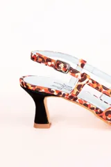 Zapato de tacón destalonado con estampado animal print en tonos naranja y marrón, con lazo doble en la parte delantera y tira trasera con hebilla. Tacón cuadrado de 2,5 cm y suela de cuero.