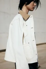 Campera de denim color crudo con cuello de pana color beige, con botones al frente, corte holgado, bolsillos superiores y bolsillos parche delanteros, hombros caídos y puños abotonados.