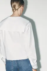 Camisa blanca de algodón con cuello bobo, manga larga con puños y cierre frontal con botones.