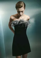 Vestido corto negro de fiesta con escote palabra de honor y adorno de plumas en el borde superior.