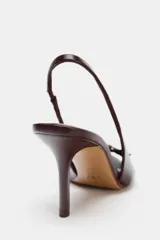 Sandalia destalonada color marrón con punta fina, tacón de aguja y tira delantera con detalle de hebilla dorada.