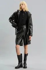 Bermuda de símil cuero brillante color negro, de calce relajado y tiro medio. Presenta bolsillos cargo laterales, bolsillos delanteros, pinzas traseras, presillas y broche delantero.