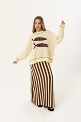 Sweater color manteca de tejido de punto con cuello redondo y ribete marrón. Presenta dos peces marrones tejidos en el frente con detalles bordados a mano.