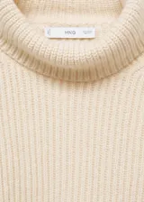 Sweater de punto grueso color crema, con cuello alto y mangas largas.